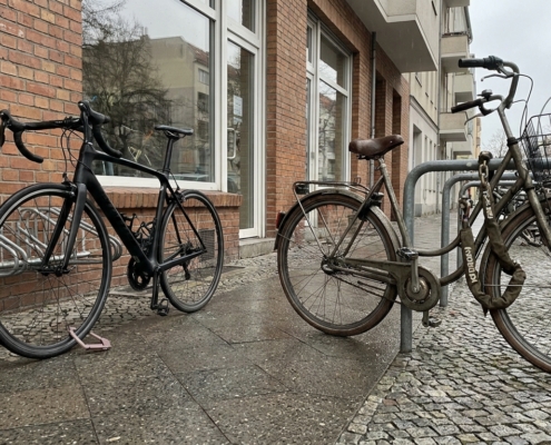 Teures Rennrad mit dünnem Faltschloss neben einfachem Stadtrad mit dickem Kettenschloss vor einem Ladengeschäft