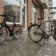 Teures Rennrad mit dünnem Faltschloss neben einfachem Stadtrad mit dickem Kettenschloss vor einem Ladengeschäft