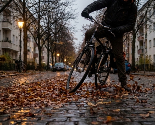 Radfahrer rutscht mit dem Vorderrad auf nassem, laubbedecktem Kopfsteinpflaster in der Dämmerung
