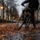 Radfahrer rutscht mit dem Vorderrad auf nassem, laubbedecktem Kopfsteinpflaster in der Dämmerung